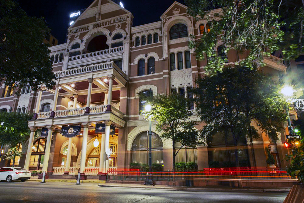 The ornate white pillared Driskill hotel against a dark night with trees on either side | Austin, TX | US Ghost Adventures