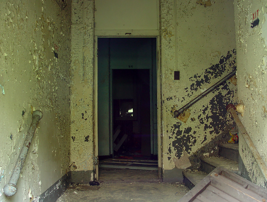 photo shows a hallway and stairwell dark and dingy, where paint is peeling.