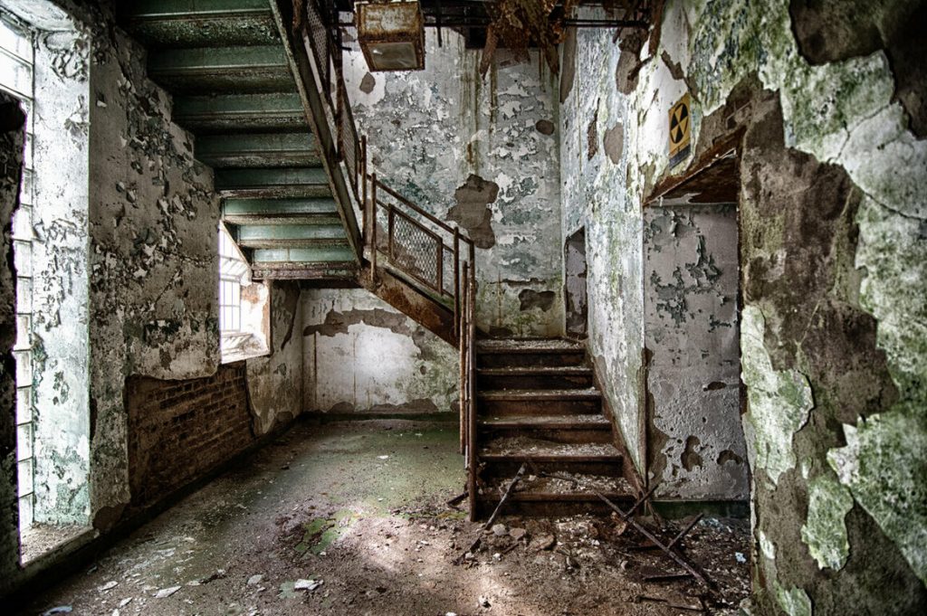 photo shows a decaying set of stairs, with peeling paint and dirt covering the floor and steps 