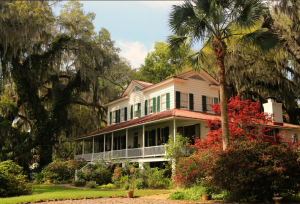Savannah's Most Haunted. green, white and pink colored house with enclosed front porch and large trees. 