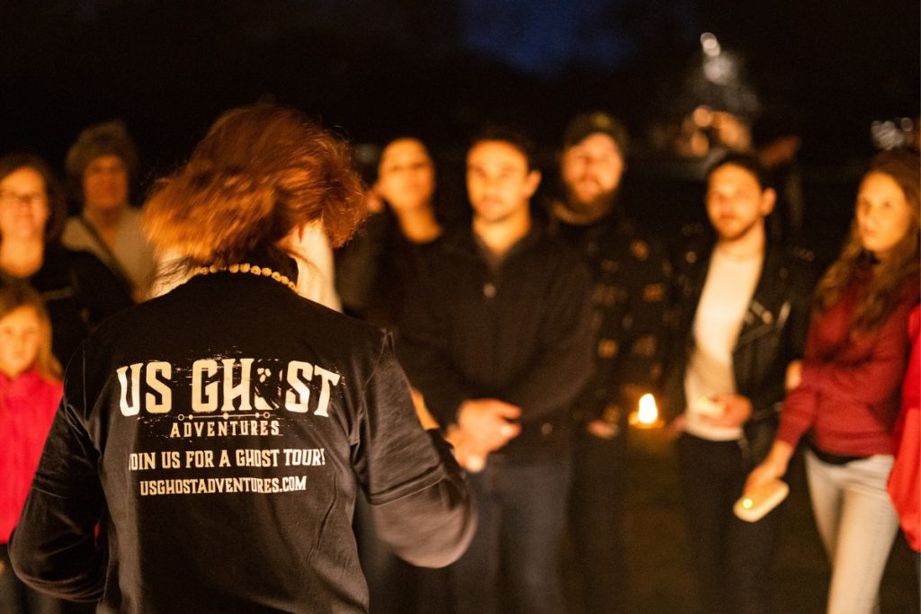 A group of guests at night in front of a guide wearing a black US Ghost Adventures tour guide shirt in San Diego during a tour.