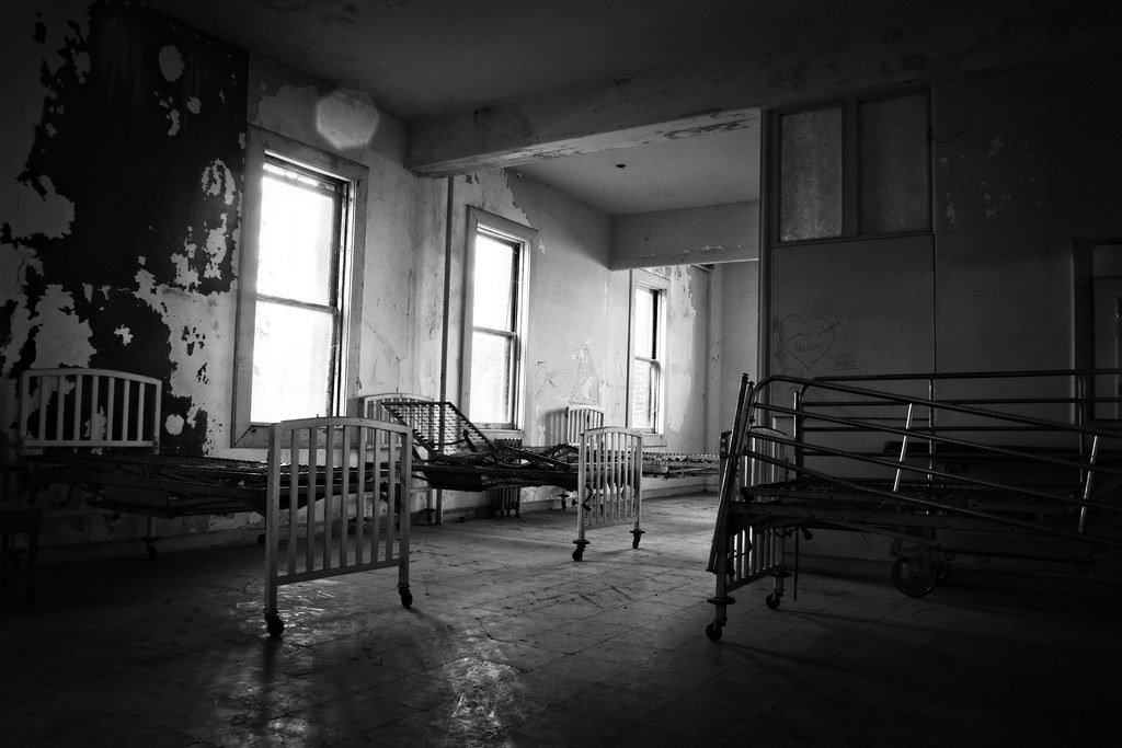 Various chairs and benches sit inside a decrepit room. Black and white photo
