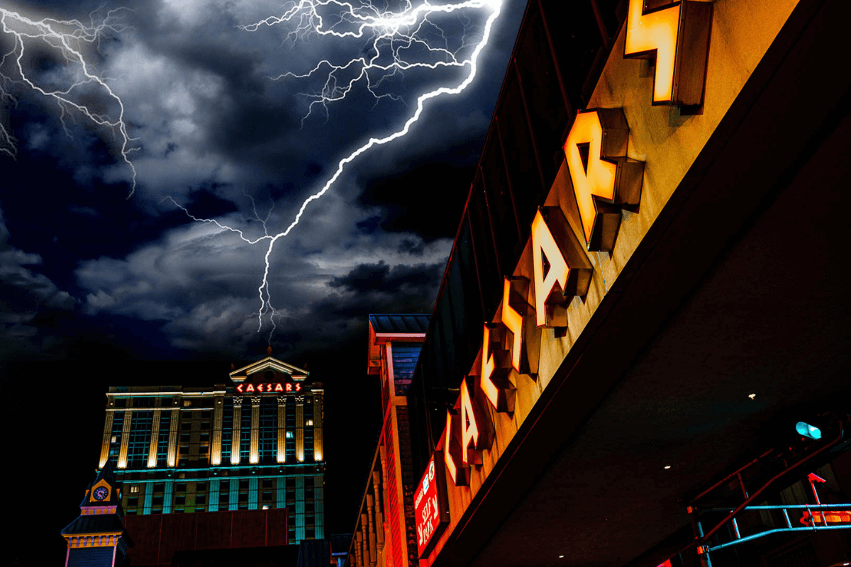 Historic multi level hotel Caesars palace with neon yellow sign against a grey and lightening filled sky.